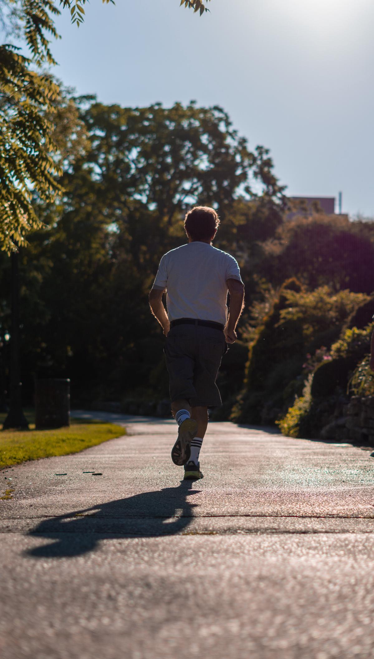 A person jogging in a park with a beautiful sunrise as the background.