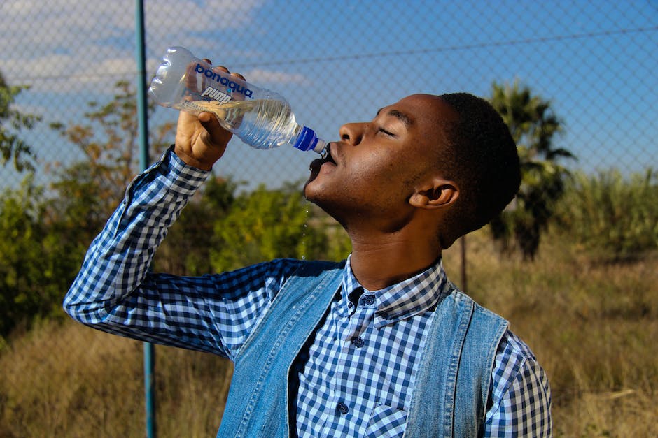 A person drinking water from a travel water bottle while hiking in a scenic mountain landscape.